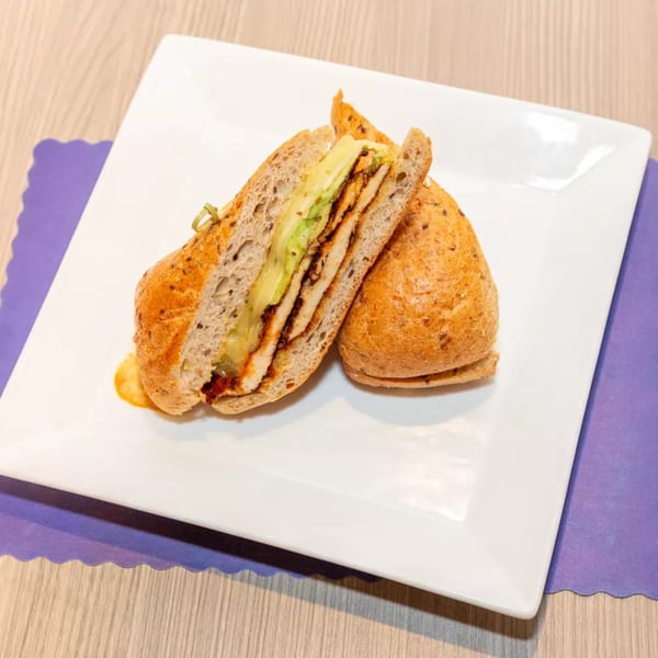 A sliced chicken and avocado sandwich on a white plate with a purple placemat.