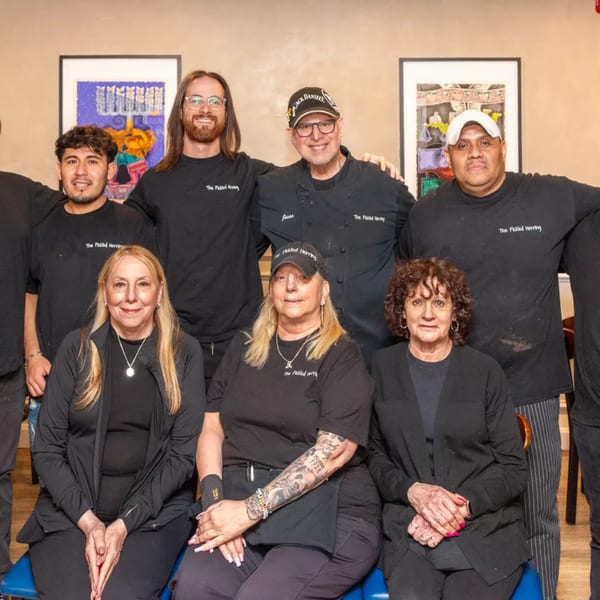 The Pickled Herring deli staff, seven smiling people in black uniforms, pose for a group photo.