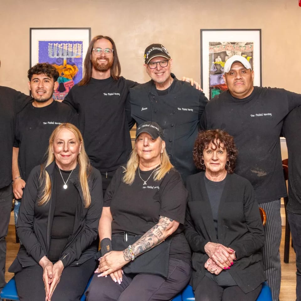 The Pickled Herring deli staff, seven smiling people in black uniforms, pose for a group photo.