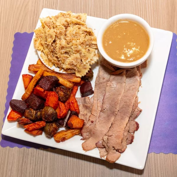 Sliced roast beef, roasted vegetables, farfalle pasta, and gravy on a white rectangular plate.