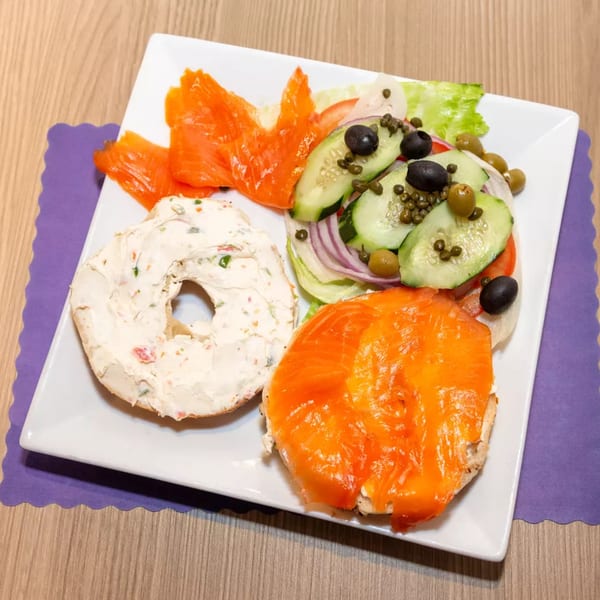 Bagel with cream cheese, smoked salmon, and a side salad with cucumbers, olives, and capers.