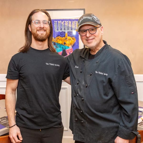 Two men, one with long hair and glasses, the other in a chef's coat, smiling at The Pickled Herring.