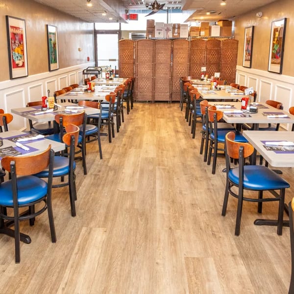 Empty restaurant dining room with rows of tables, blue chairs, and a woven room divider.