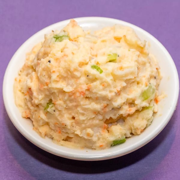 Creamy potato salad with visible chunks of potato, carrots, and green celery in a white bowl.