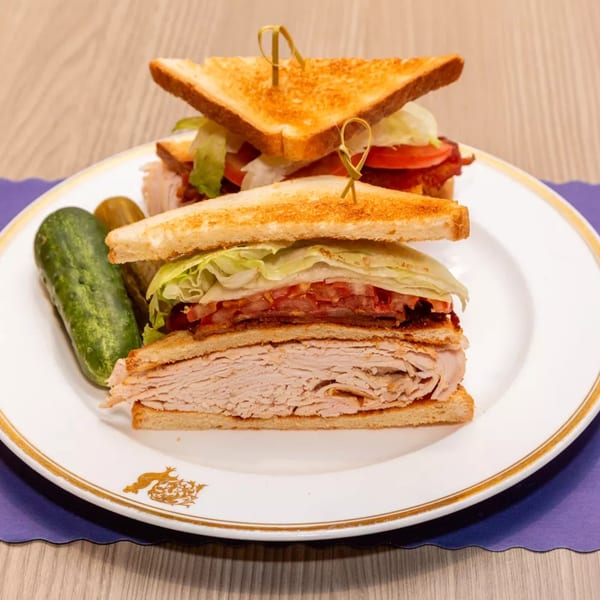 A turkey club sandwich with bacon, lettuce, and tomato, served with a pickle spear.