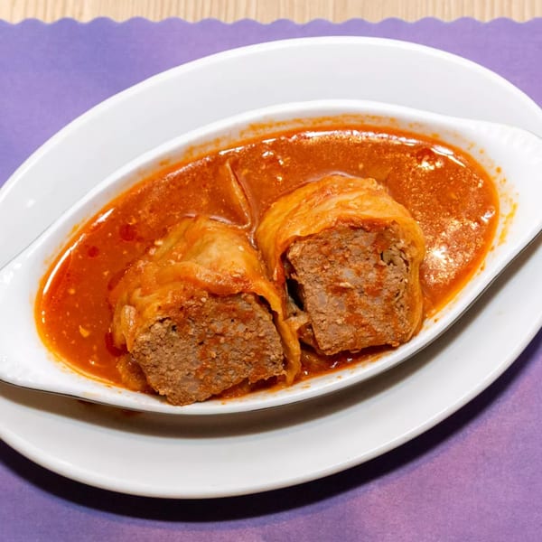 Two cabbage rolls, cut open to show the meat filling, in a rich red sauce on a white dish.