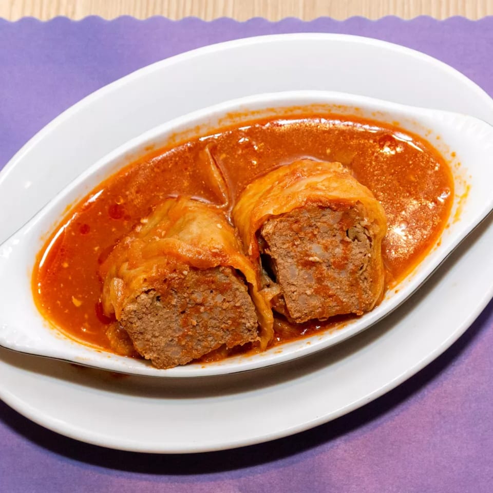 Two cabbage rolls, cut open to show the meat filling, in a rich red sauce on a white dish.