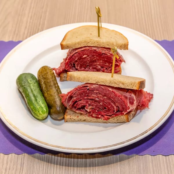 Two corned beef sandwiches on rye bread with two pickles on a white plate.