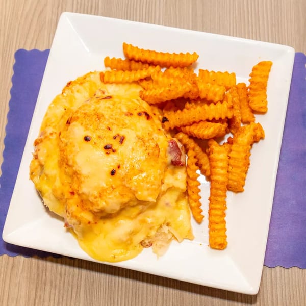 Cheesy chicken and bacon dish with a side of seasoned crinkle-cut fries on a white plate.