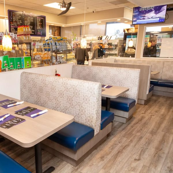 Interior of a diner with blue and patterned booths, light wood tables, and a menu board.